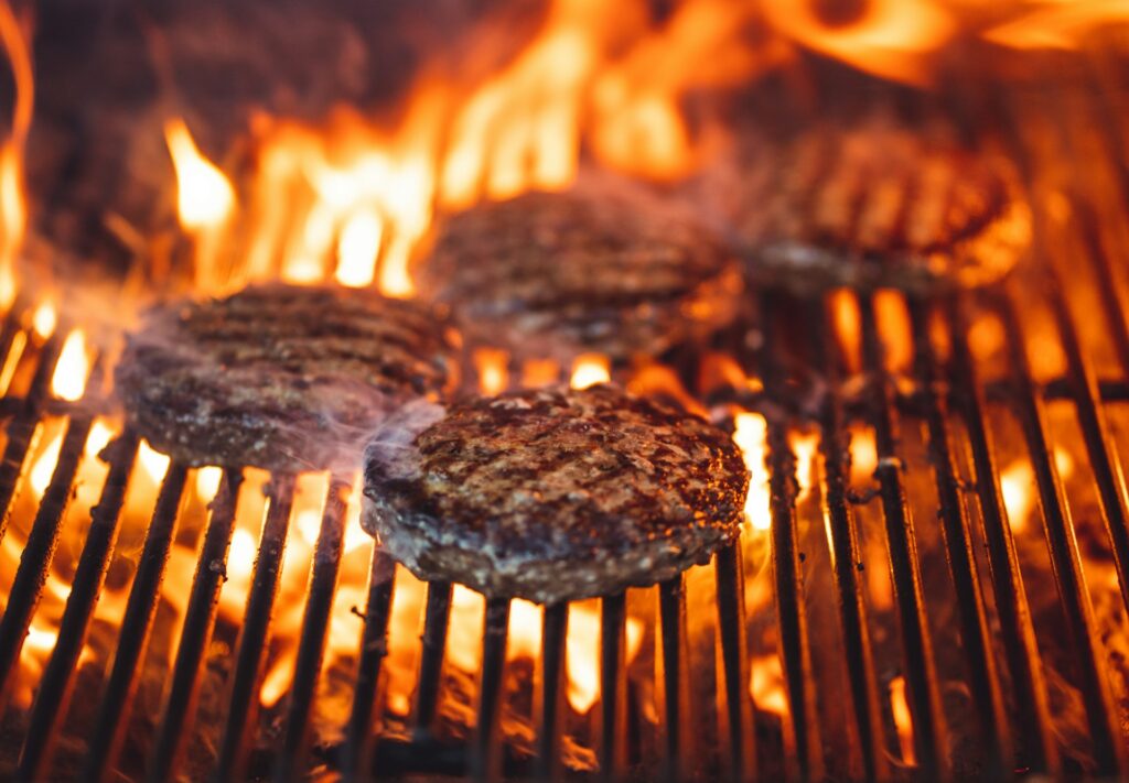 Burger patties cooking on a flaming grill